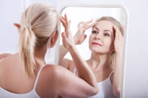 Mature woman looking in mirror and considering having a facelift