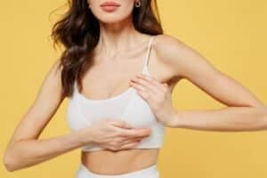 Woman in bra holding one of her breasts with implant and considering removal