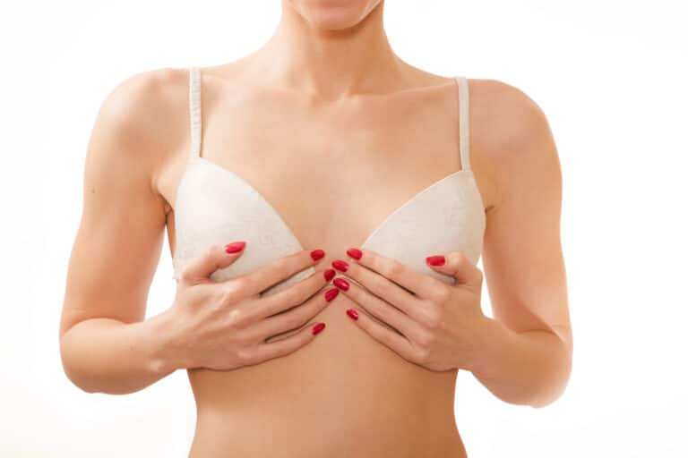 Woman in a white bra covering her breasts with both hands after breast implant removal
